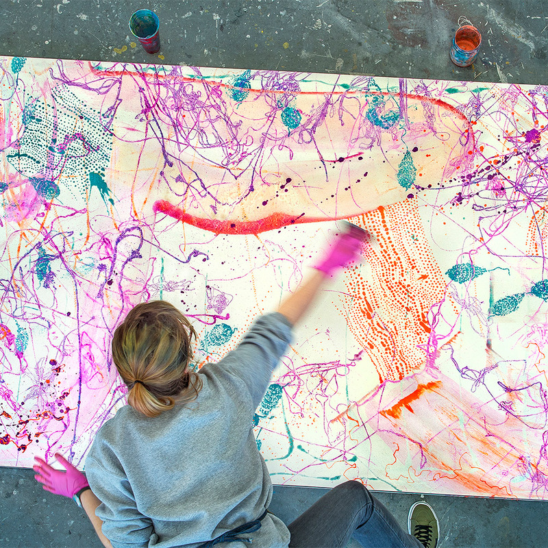 A student creating a large, abstract, colorful painting