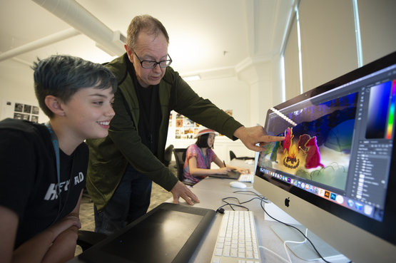 An instructor looks at a students digital work on the computer. 