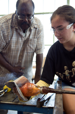 An instructor helps a student with their glass project. 