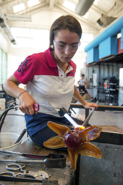 A Pre-College student using a blow torch to shape their glass form. 