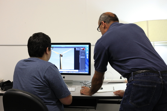 An instructor looks at a student's graphic design project in a computer lab. 
